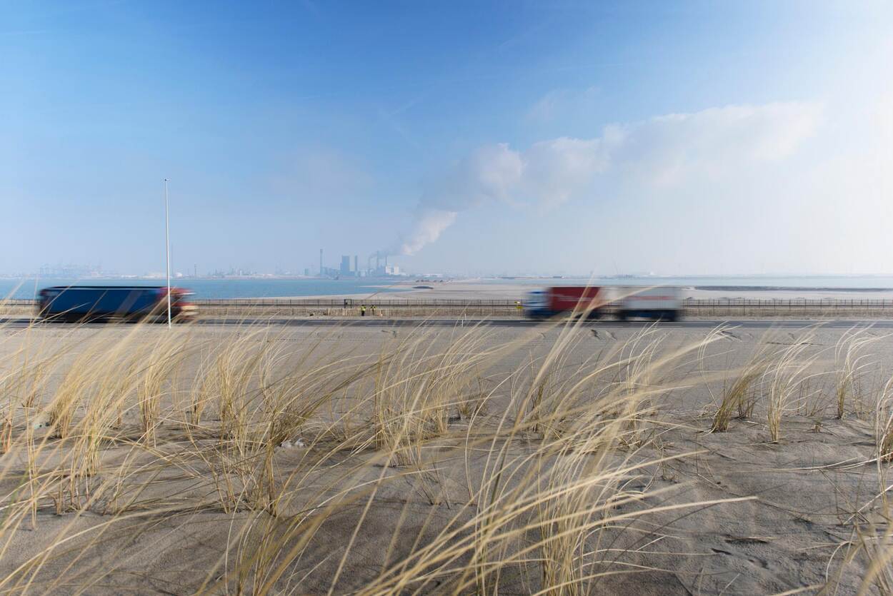 A road with two trucks, blurred from movement, with a factory emitting smoke in the background.