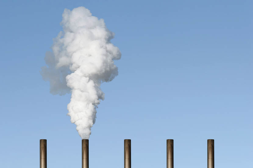 5 chimneys against a blue sky. One of them is emitting smoke.